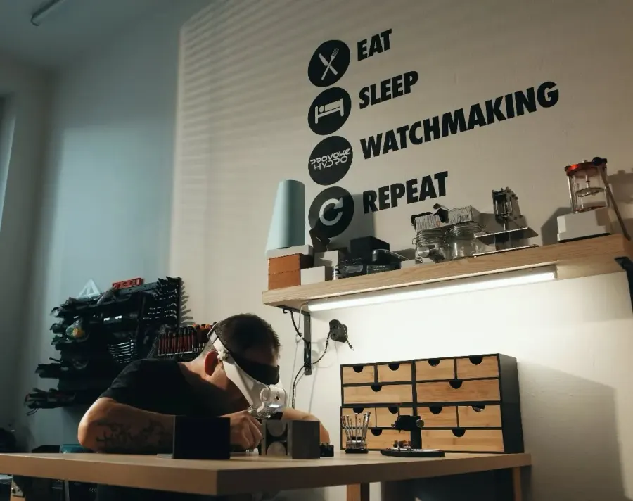 Hodinář při práci v dílně PROVOKE, na stěně nápis Eat Sleep Watchmaking Repeat